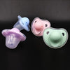 A set of two silicone pacifiers in light blue and pink with protective covers displayed against a dark background.