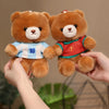 A hand is holding two teddy bears wearing football jerseys, one blue and white with the number 10, and another red with the n