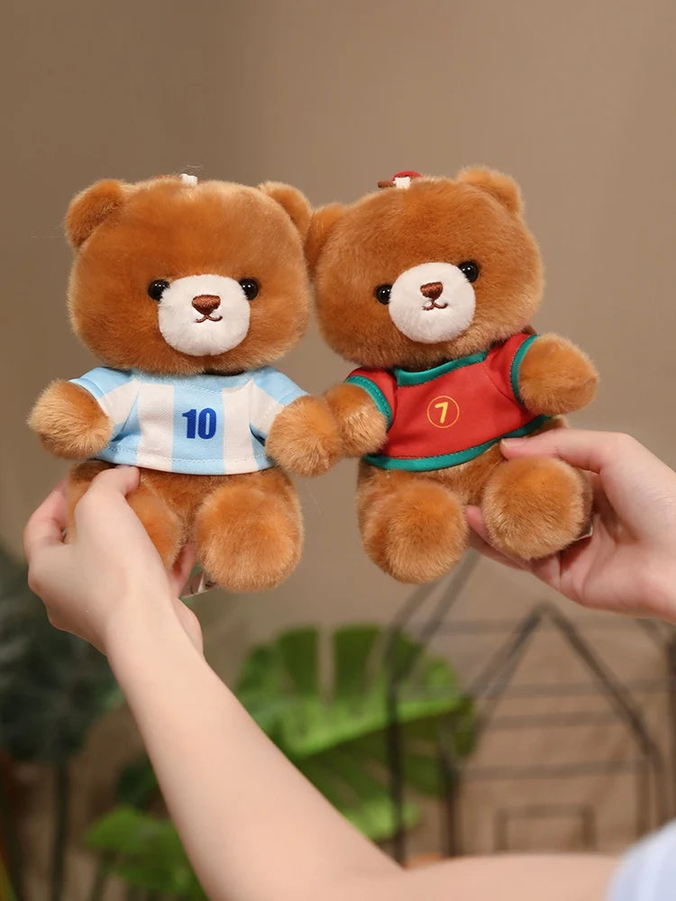 A hand is holding two teddy bears wearing football jerseys, one blue and white with the number 10, and another red with the n