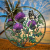 A round acrylic window hanging featuring a detailed illustration of purple Scottish thistles and foliage against a sunset sky