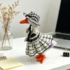 A white goose statue wearing a black and white plaid dress and a checkered hat, standing on a white surface.