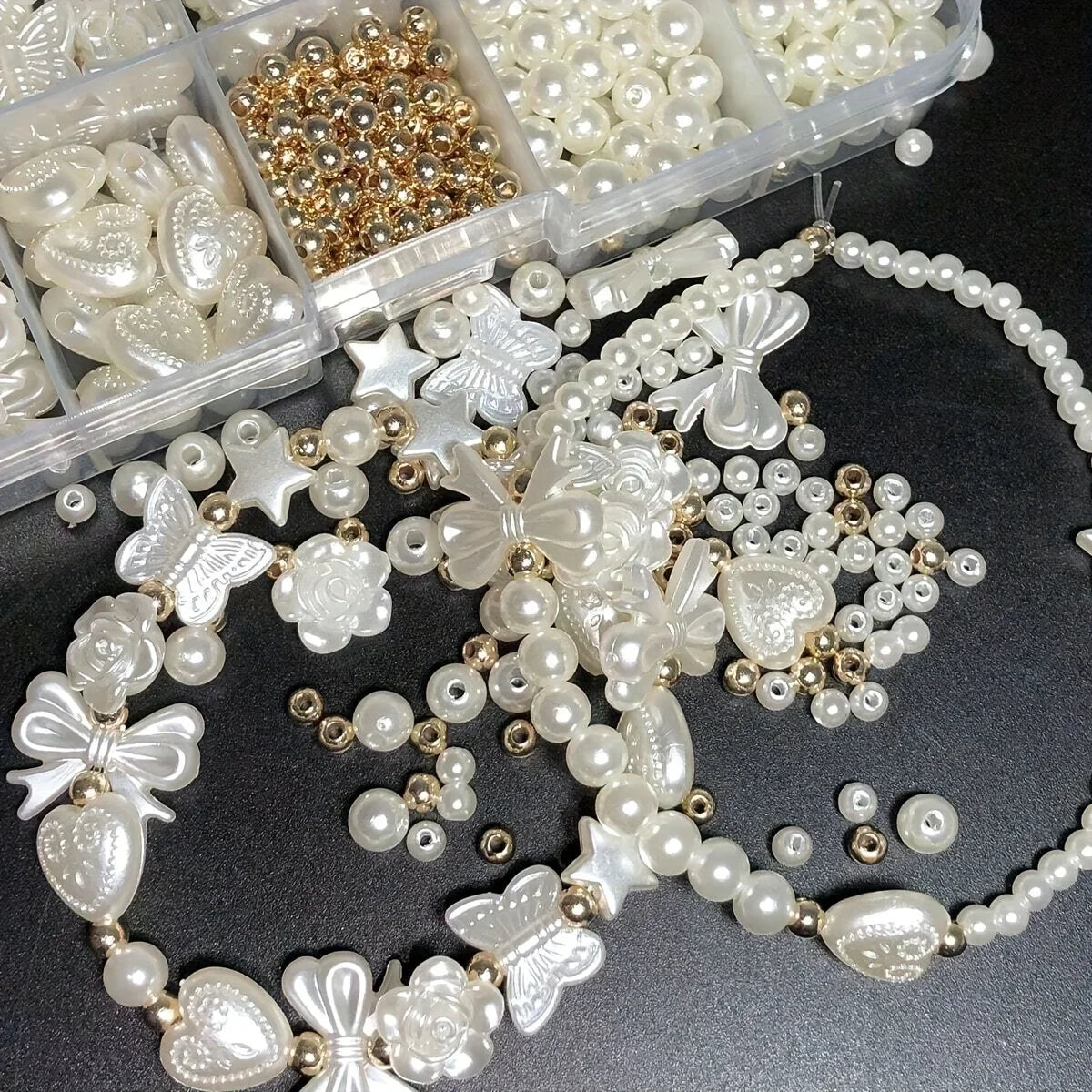 A collection of white and gold acrylic pearl beads, including hearts, flowers, and butterflies, for jewelry making.
