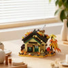 A miniature wooden cabin building set with a green roof and yellow walls sits on a light wood surface.