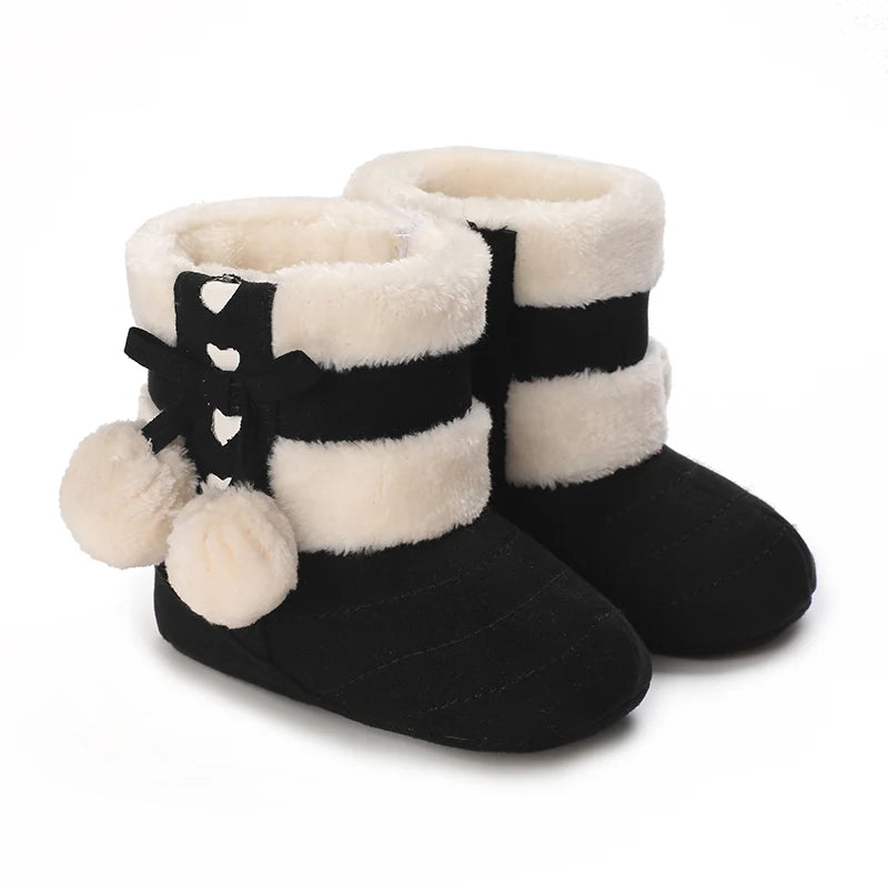 A pair of black and cream faux fur baby first walker shoes with a decorative black bow detail.