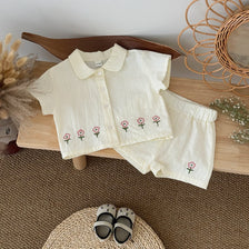 A cream baby cotton shirt and shorts set with a pink flower pattern laid out on a wooden surface.