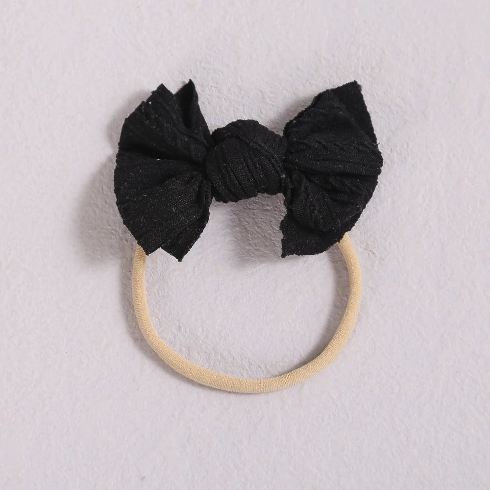 Black fabric bow headband with a light beige elastic band on a white background.