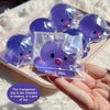 A clear plastic bag containing a purple squishy bubble squid stress relief toy is held in a hand.
