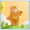 A fluffy brown Care Bear figurine with a yellow flower detail standing on green grass.