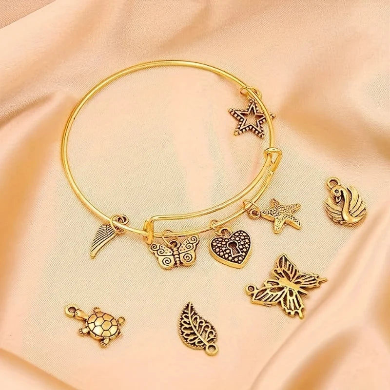 A gold-tone jewelry making kit featuring adjustable bangles and charms displayed on a soft pink fabric.