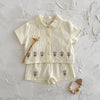 A cream baby cotton shirt and shorts set with a pink flower pattern laid flat on a white surface.