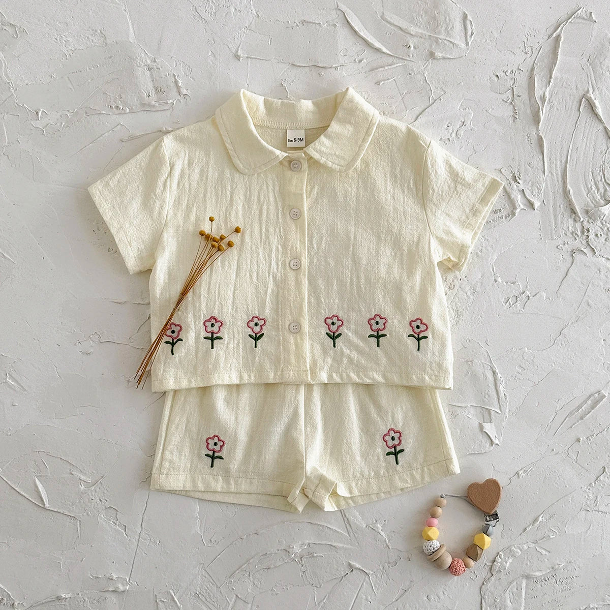 A cream baby cotton shirt and shorts set with a pink flower pattern laid flat on a white surface.