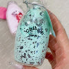 A hand holds a clear glass bottle filled with a light blue speckled liquid and a cork stopper, labeled Chiboki.