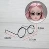 A pair of black metal round glasses frames shown next to a doll's face.