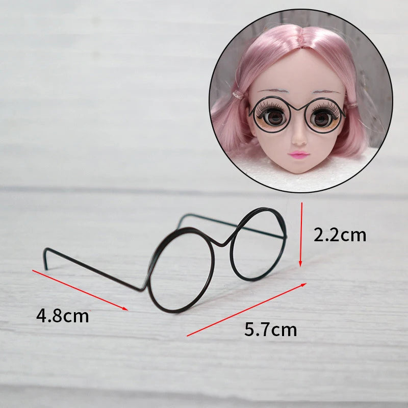A pair of black metal round glasses frames shown next to a doll's face.