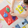 A child is using an acrylic clay roller and sheet set to sculpt various colored clay pieces on a red surface.