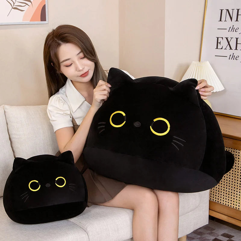 A woman is holding a large black cat plush toy and a smaller black cat plush toy on a light-colored sofa.