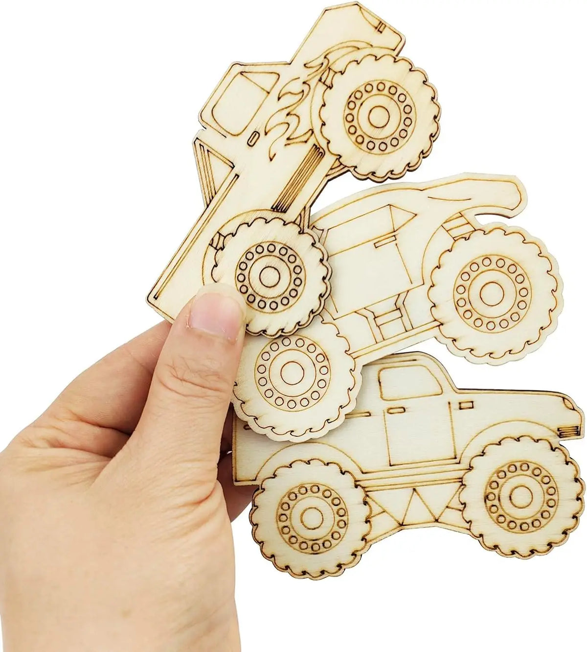 A hand holds several unfinished wood monster truck cutouts for DIY crafts.