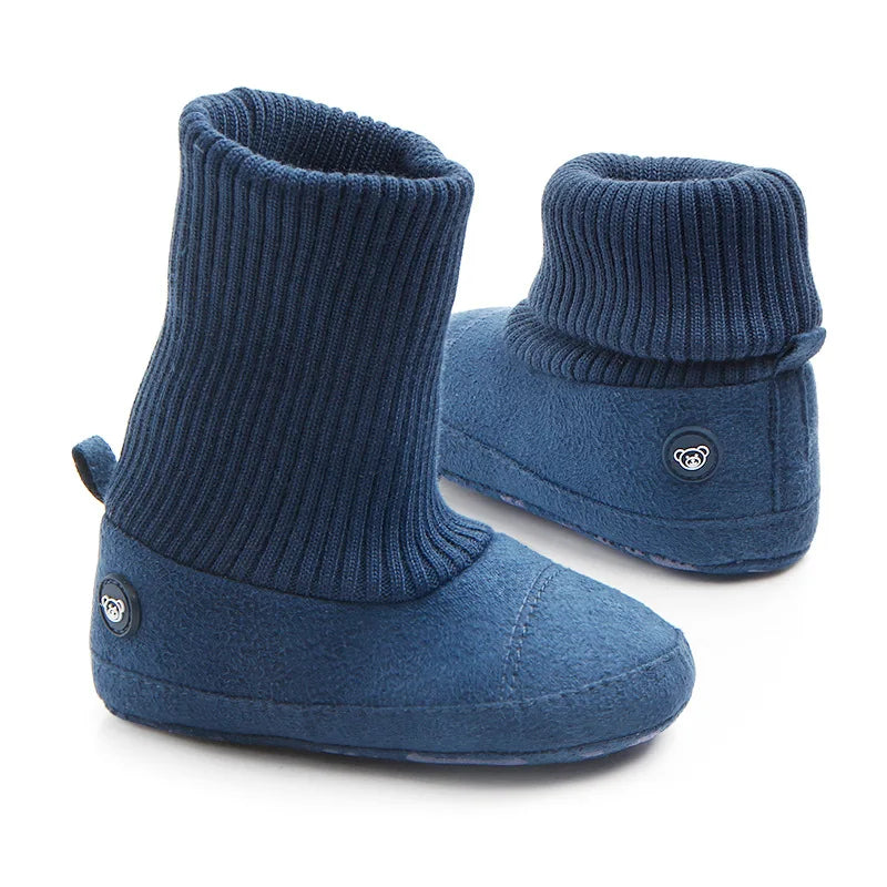 A pair of navy blue baby winter snow boots with ribbed knit texture and fuzzy ball accents.