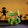 A bright green plush monster doll with large teeth and orange eyes is displayed against a dark background.