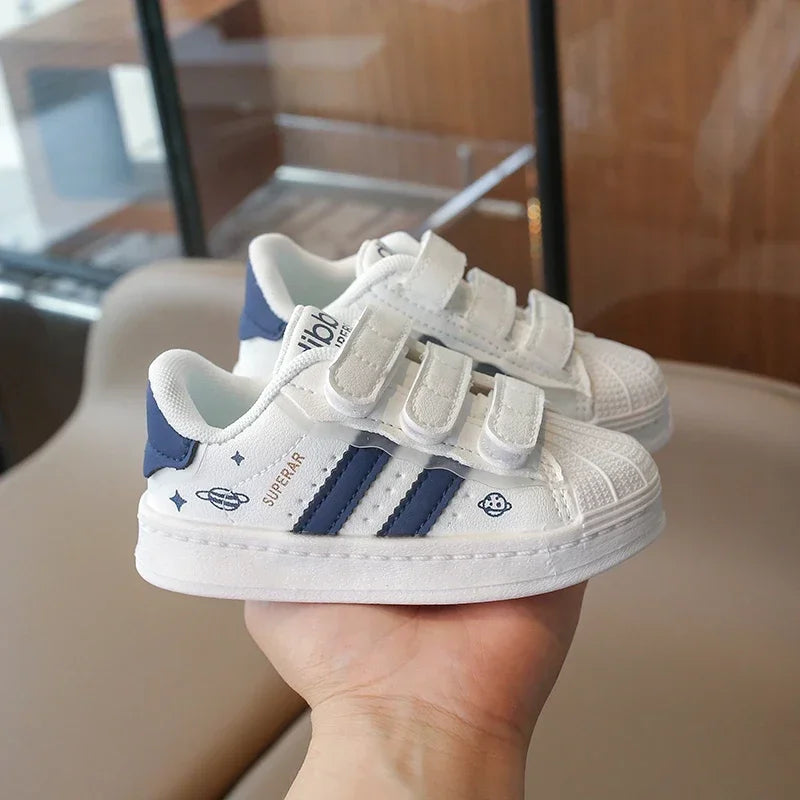 A pair of white and navy casual sneakers with hook-and-loop closure are held in a person's hand.