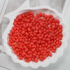 A white oval dish filled with bright red oval glass rice grain beads for jewelry making
