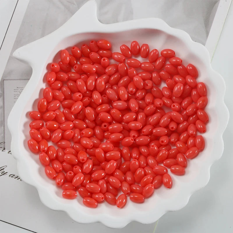 A white oval dish filled with bright red oval glass rice grain beads for jewelry making