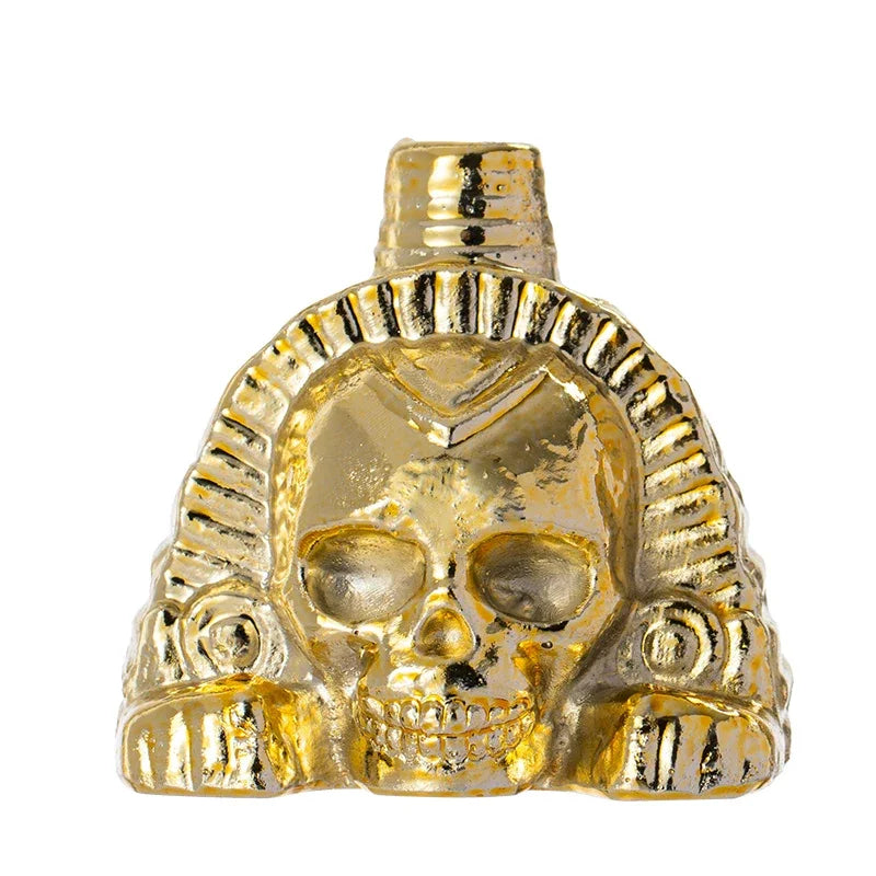 A handcrafted gold Aztec death mask or whistle featuring a stylized skull and elaborate headdress.
