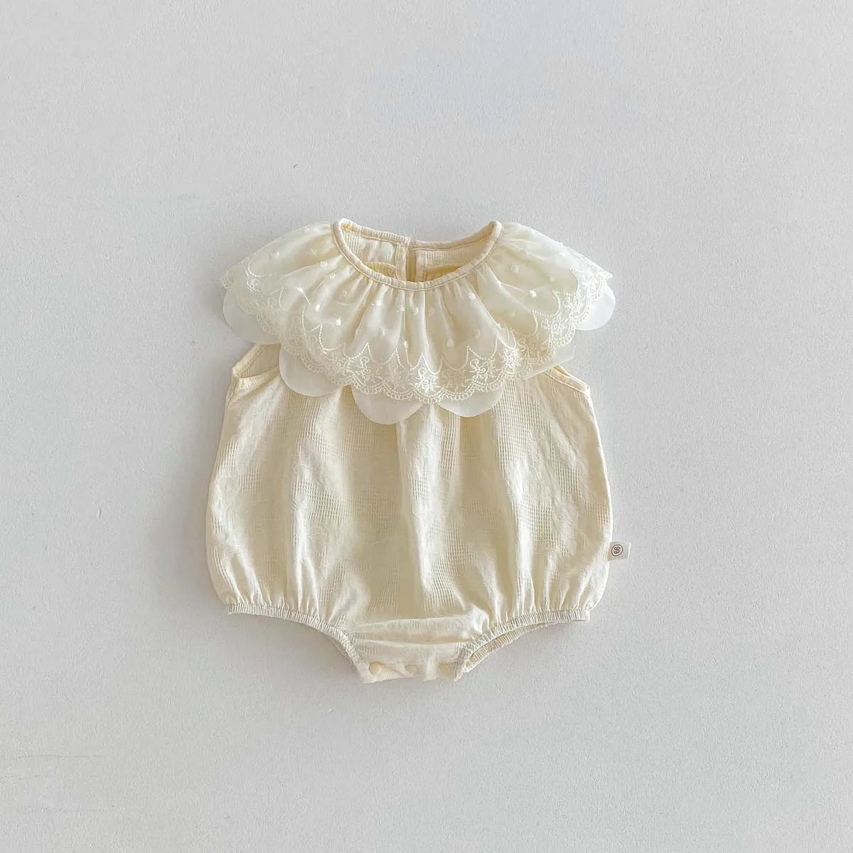 A cream-colored baby girl sleeveless jumpsuit with a delicate lace collar and gathered fabric details.