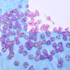 A pile of small purple glass beads shaped like lily of the valley flowers scattered on a white surface.