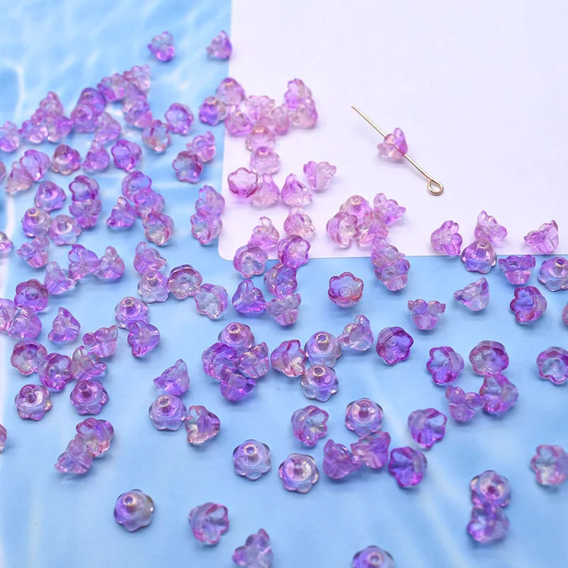 A pile of small purple glass beads shaped like lily of the valley flowers scattered on a white surface.
