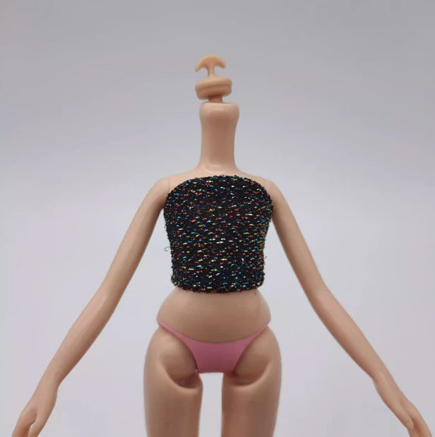 A fashion doll wearing a black sequined top and pink panties, standing against a light gray background.