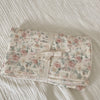 A folded 100% cotton muslin swaddle blanket with a floral print lying on a white textured surface.
