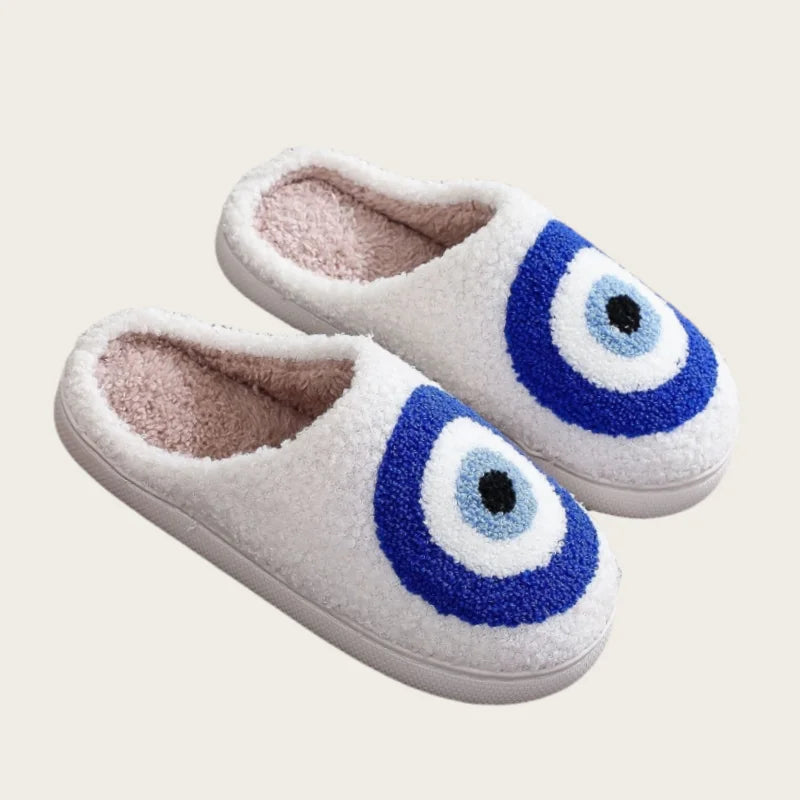 A pair of white plush indoor slippers with blue circular designs.