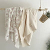 A cream colored muslin swaddle blanket with a pink floral print is hanging on a wooden rod.
