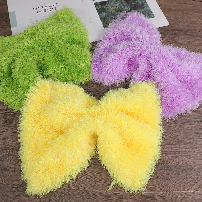 Three fluffy faux fur yarn skeins in lime green, purple, and yellow displayed on a wooden surface.