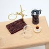 A miniature hand-brewed coffee stand set for dollhouse featuring a brass coffee filter and a small dark coffee pot.