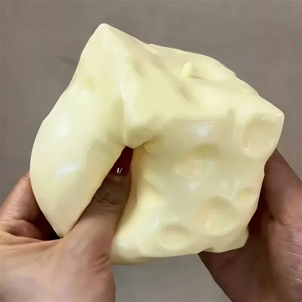 A hand holds a large, pale yellow squishy cheese cube fidget toy.