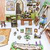 A collection of miniature wooden items and painted scenes arranged on a green moss background.