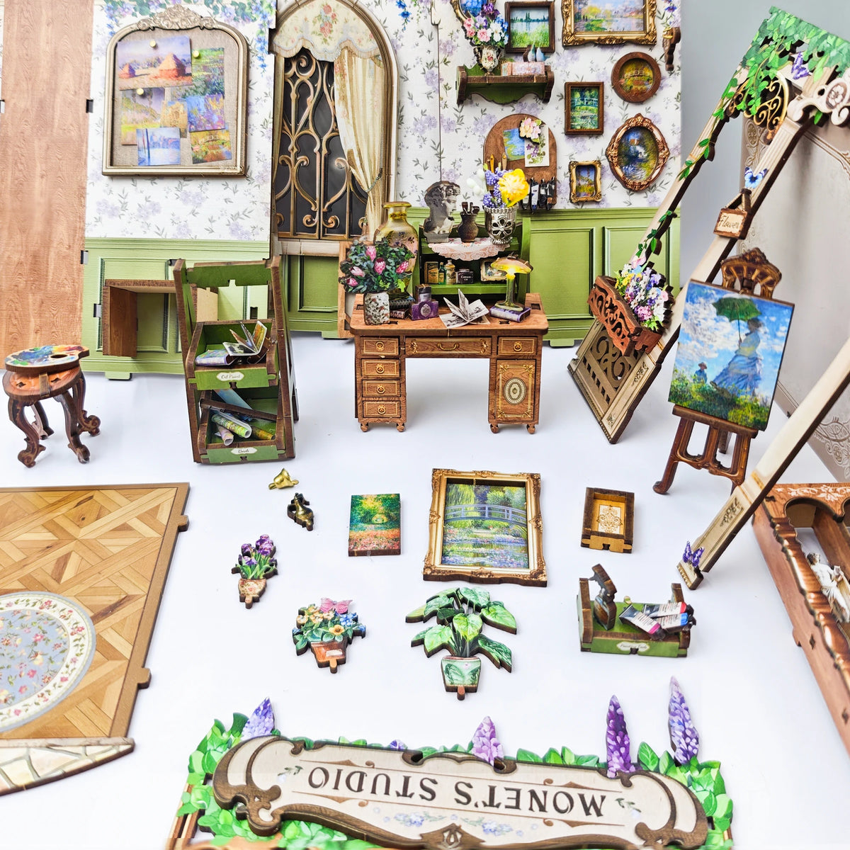 A collection of miniature wooden items and painted scenes arranged on a green moss background.