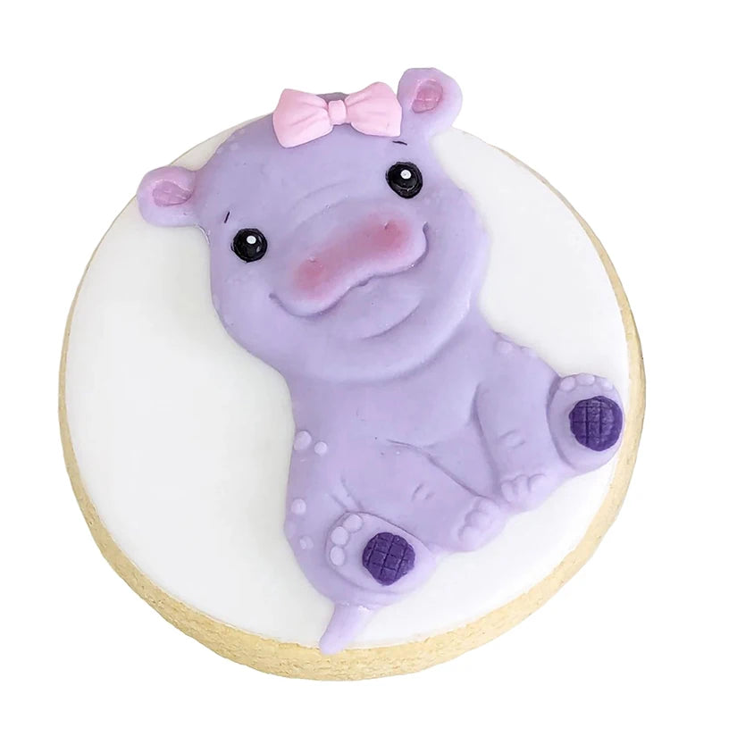 A cute purple elephant silicone baking mold with a pink bow, resting on a round wooden surface.
