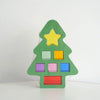 A green acrylic building block shaped like a Christmas tree with a yellow star and colored square blocks.