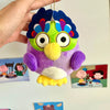 A purple and green plush toy of an owl with bright blue feathers and large eyes is being held by a hand.