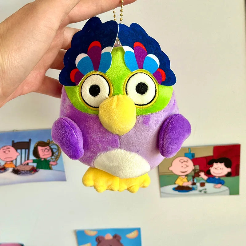 A purple and green plush toy of an owl with bright blue feathers and large eyes is being held by a hand.