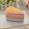 A colorful rainbow layer cake squishy toy with orange topping resting on a white lace doily.