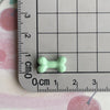 A small, light green resin bone charm is placed on a ruler marked in centimeters.