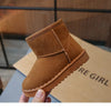 A close-up of a tan suede slip-on winter boot for a child, held against a brown cardboard box.