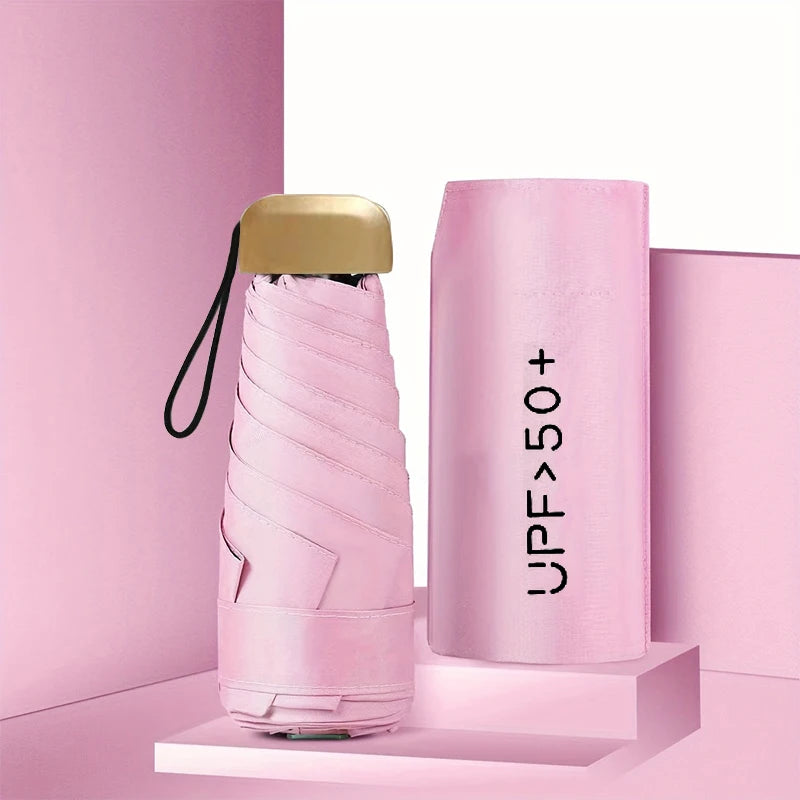 A pink compact 5-fold sun and rain umbrella with a gold-colored handle displayed on a light pink surface.
