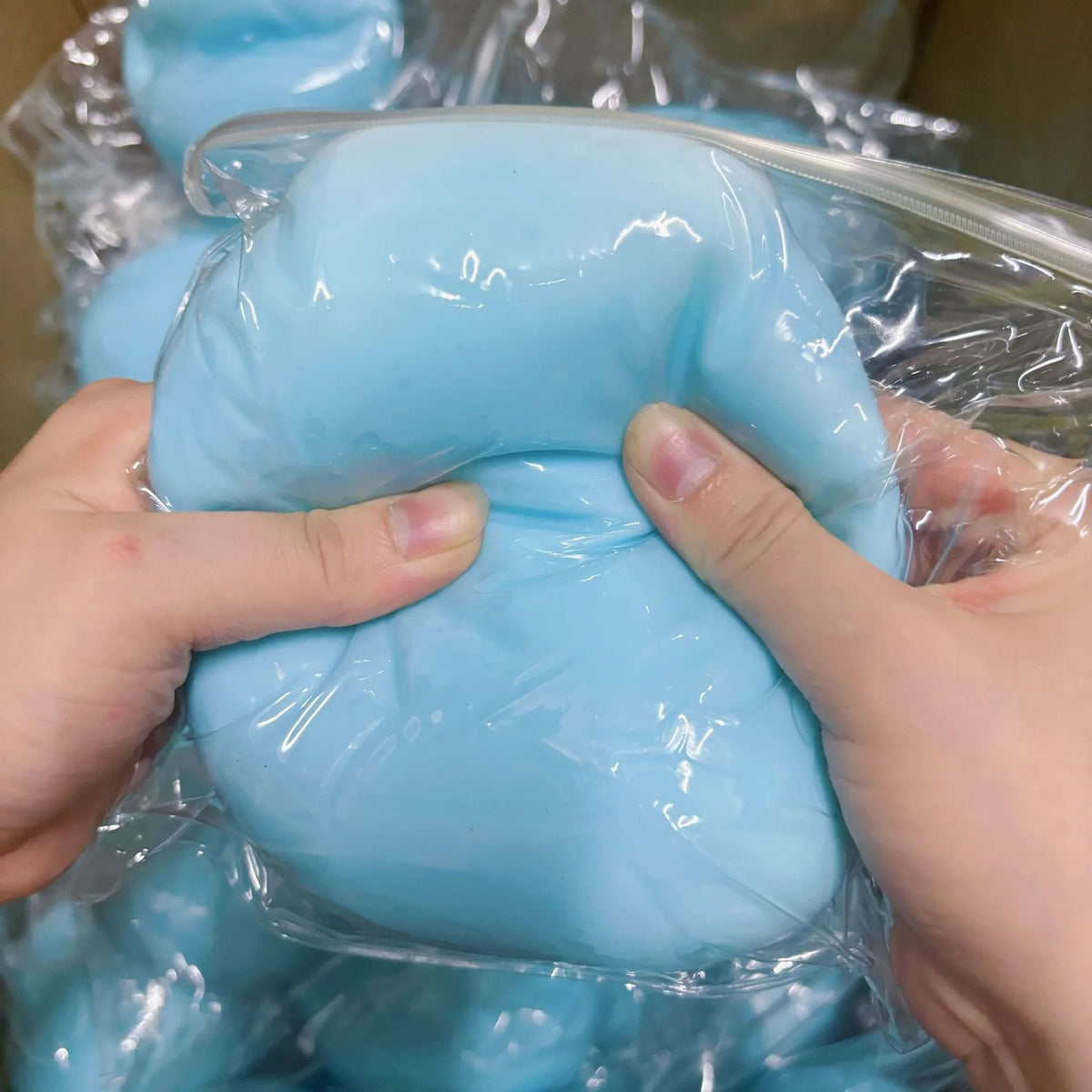 Eine Hand drückt einen hellblauen, weichen Stressball-Fidget-Spielzeug in klarem Plastik verpackt.