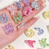 A hand holds various colorful acrylic alphabet beads in purple, pink, and green shades for crafting.