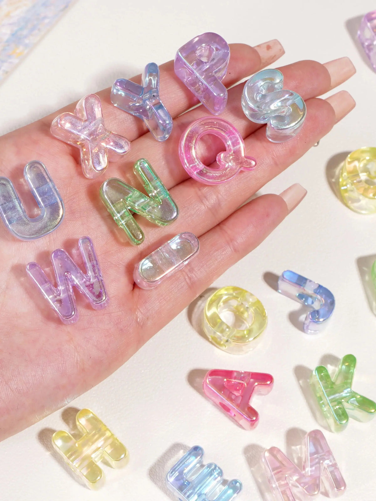 A hand holds various colorful acrylic alphabet beads in purple, pink, and green shades for crafting.